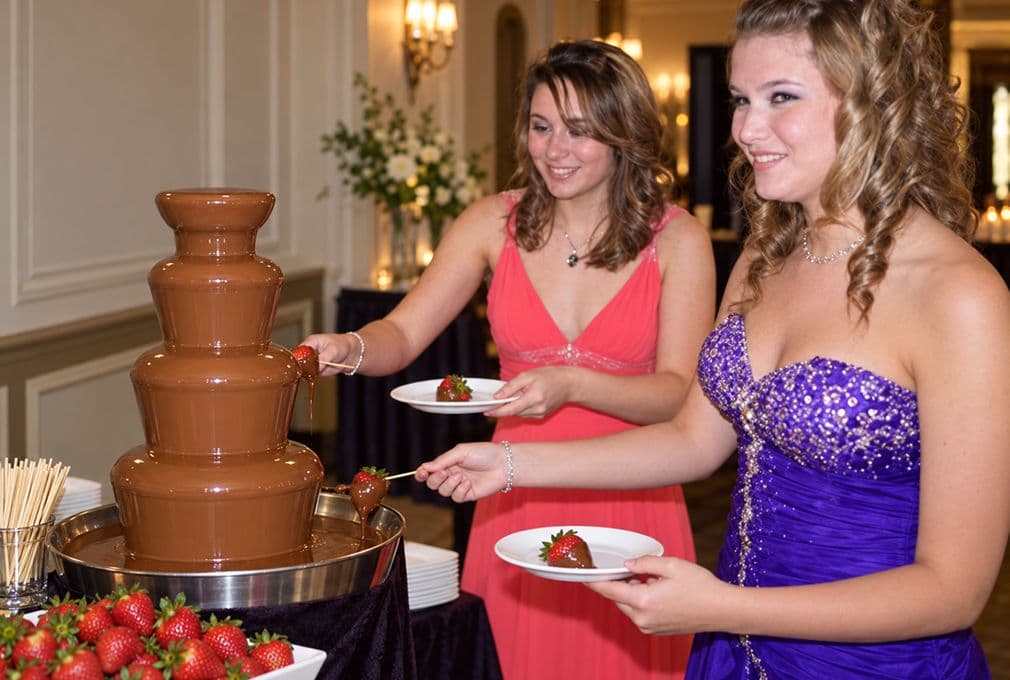 Guests dipping strawberries at a chocolate fountain during a party