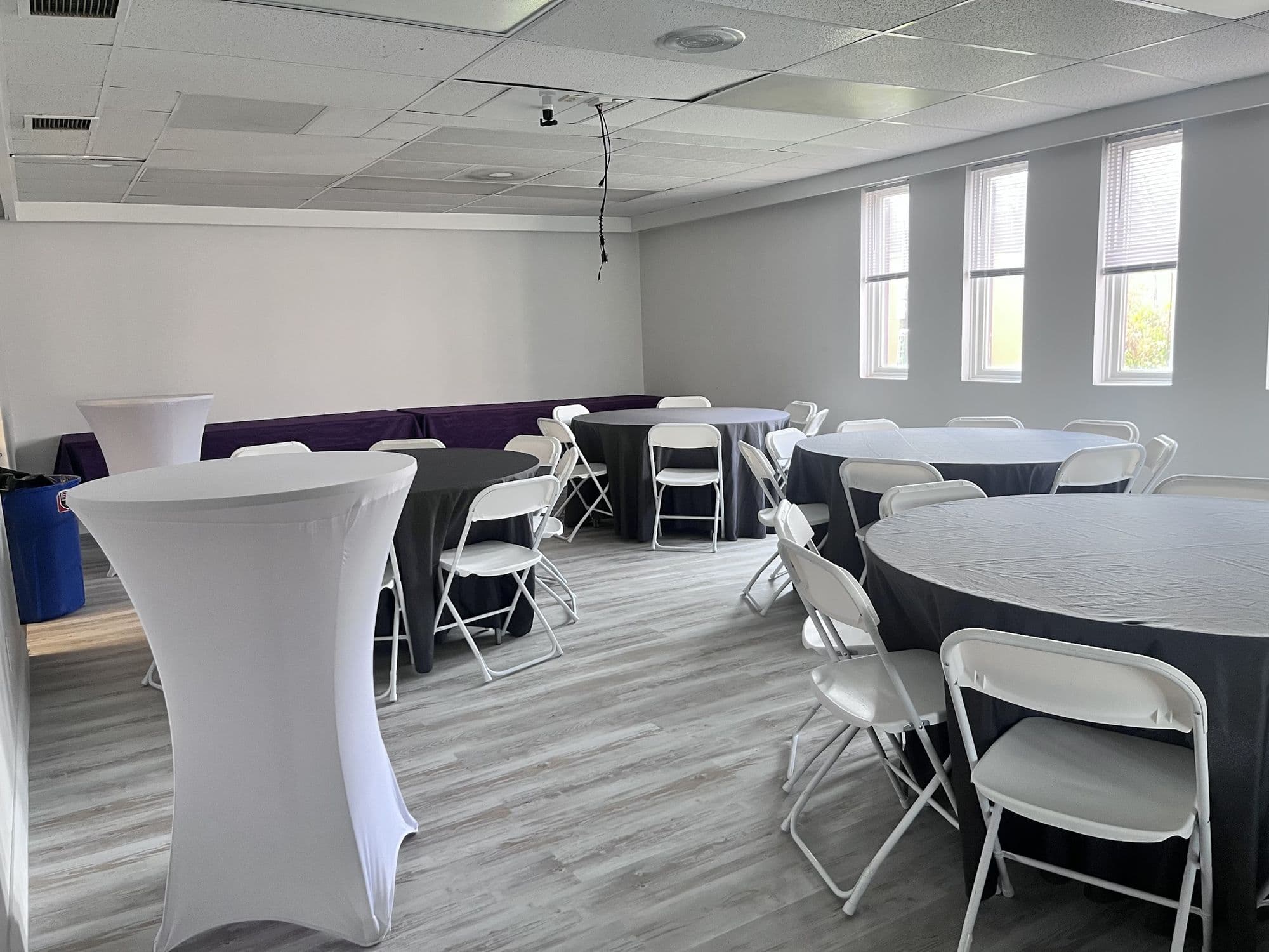 Cocktail tables in white spandex covers beside round tables set for a party in Cheektowaga