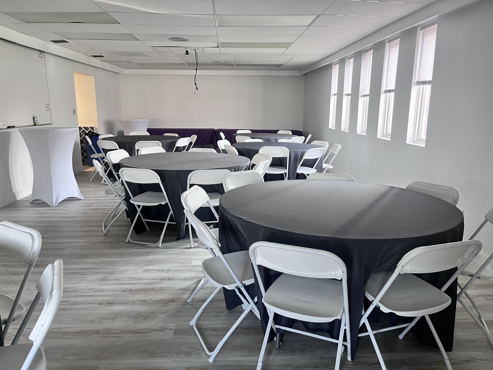 Round tables with black linens beside tall windows in the Cheektowaga event room