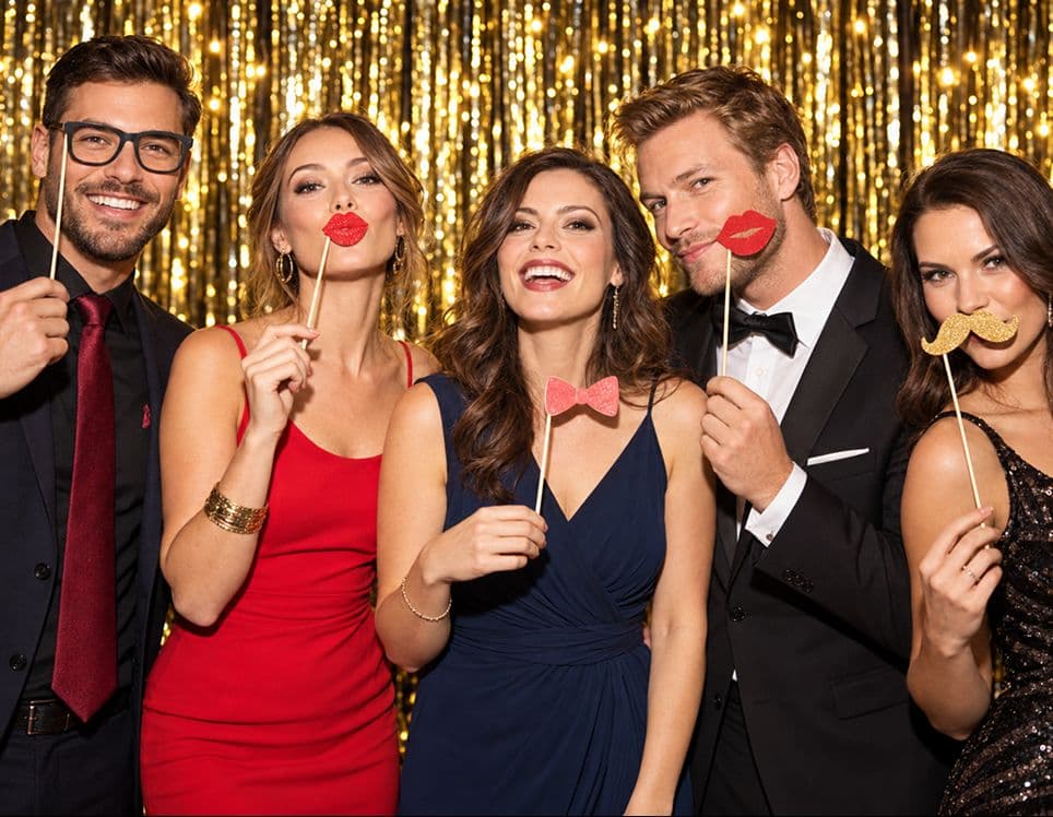 Party guests posing with photo booth props in front of a gold backdrop